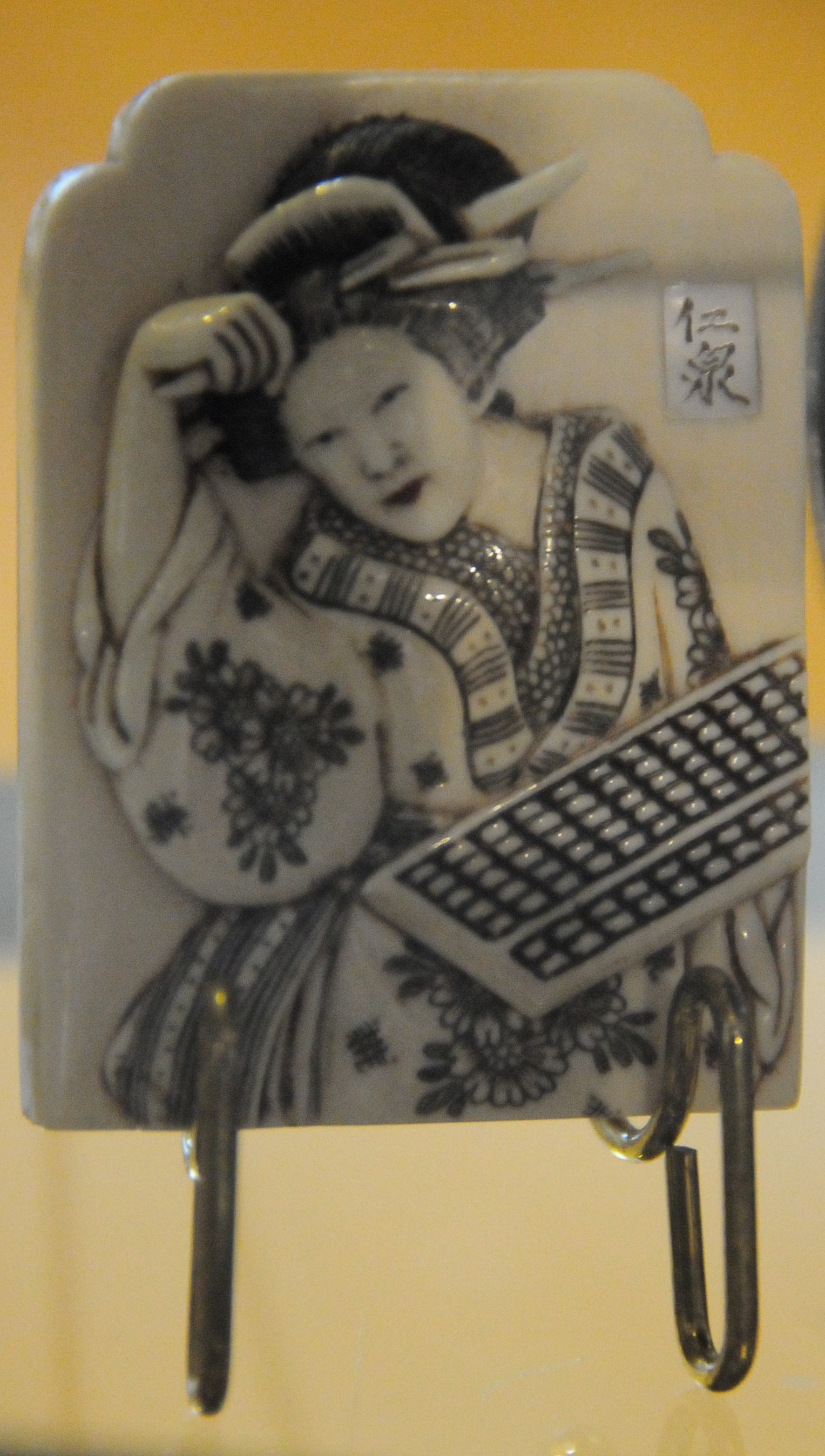 piece of ceramic jewelry depicting a woman holding a soroban